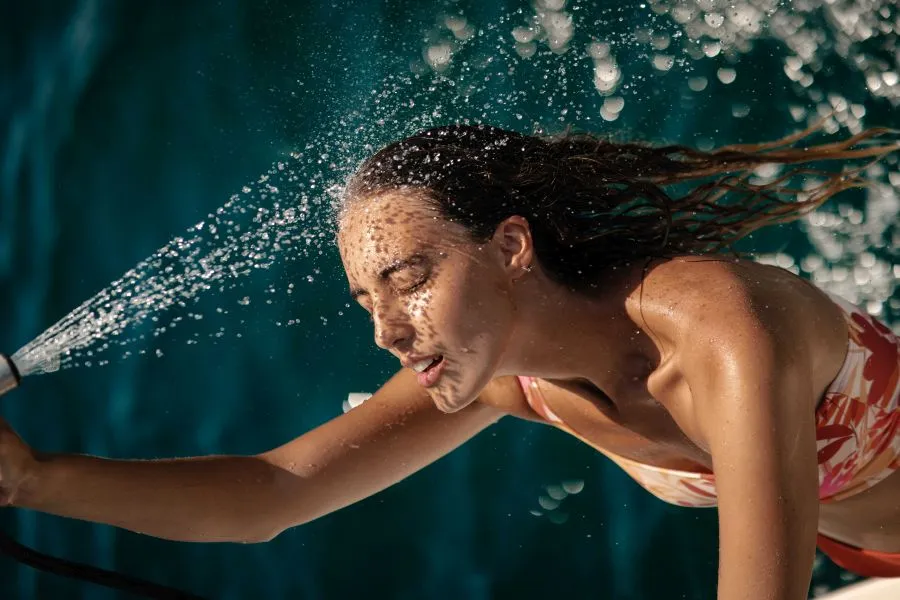 erotikus magazin fotózáson, bikinis modell zuhanyzik a medence szélén.